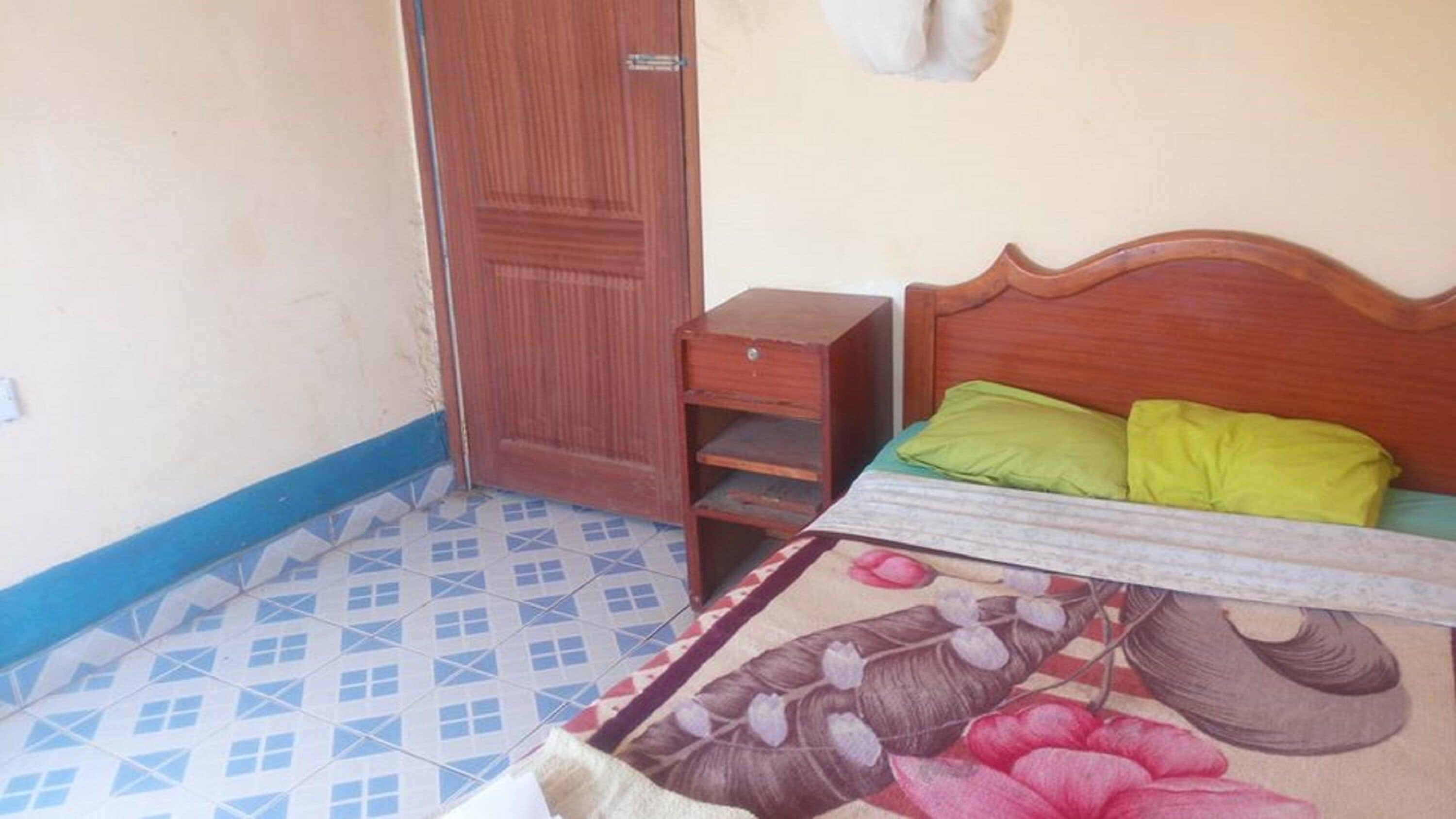 A bedroom with a wooden bed, two pillows, a small wooden nightstand, and a patterned bedspread.