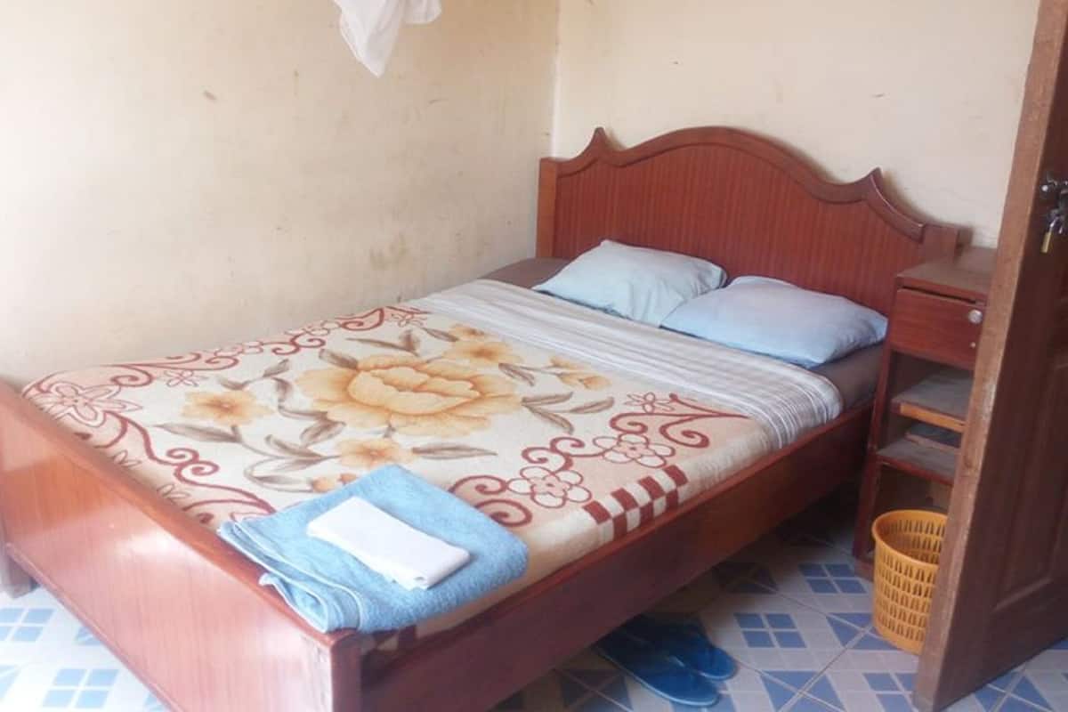 Uma cama de solteiro com colcha florida, uma mesa de cabeceira com abajur e um guarda-roupa de madeira.