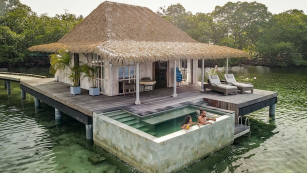 A thatched-roof bungalow with a pool and lounge chairs on a floating platform. - NAYARA Bocas del Toro (Isla Frangipani)