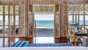 A wooden room with a bed, a chair, and a view of the sea through large glass doors. - NAYARA Bocas del Toro (Isla Frangipani)