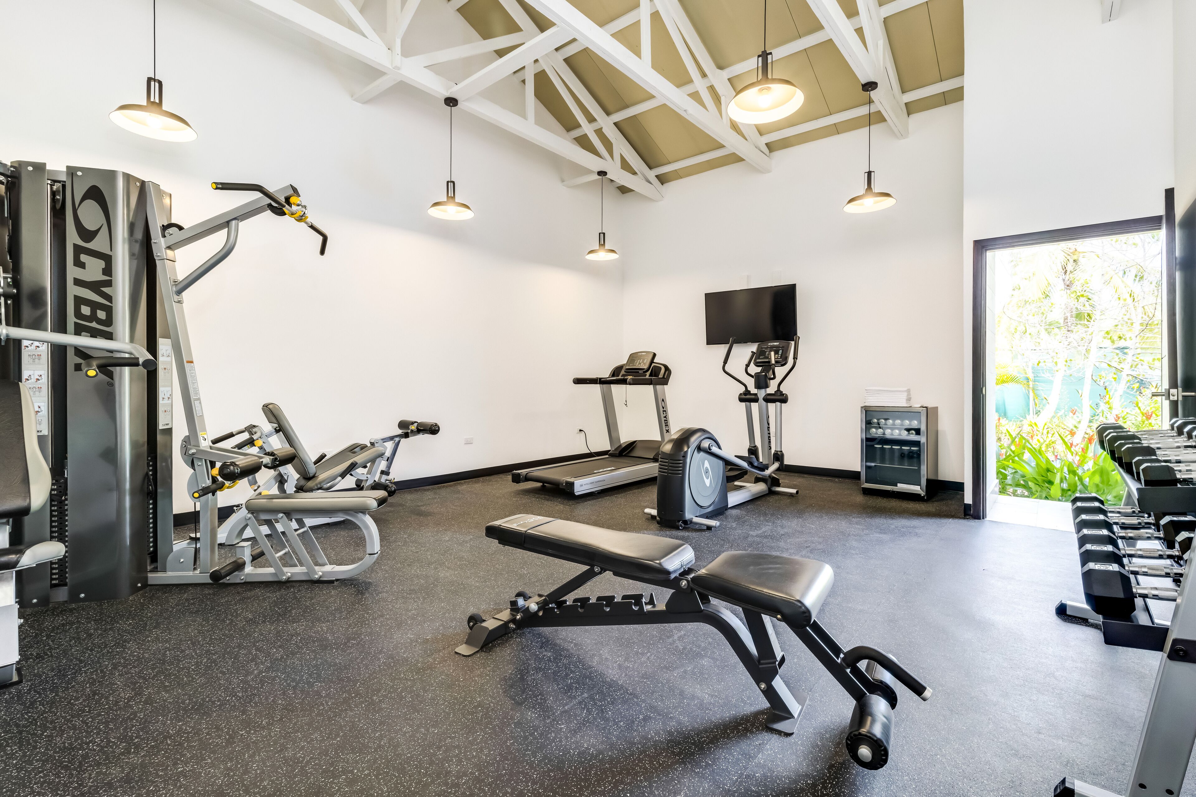 A gym with various exercise equipment, a bench, and dumbbells.