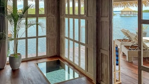 A room with large windows overlooking a water body, wooden flooring, and a potted plant. - NAYARA Bocas del Toro (Isla Frangipani)