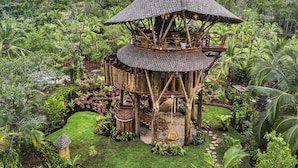 A multi-level wooden structure with a thatched roof, surrounded by lush tropical vegetation and a view of a distant body of water. - NAYARA Bocas del Toro (Isla Frangipani)