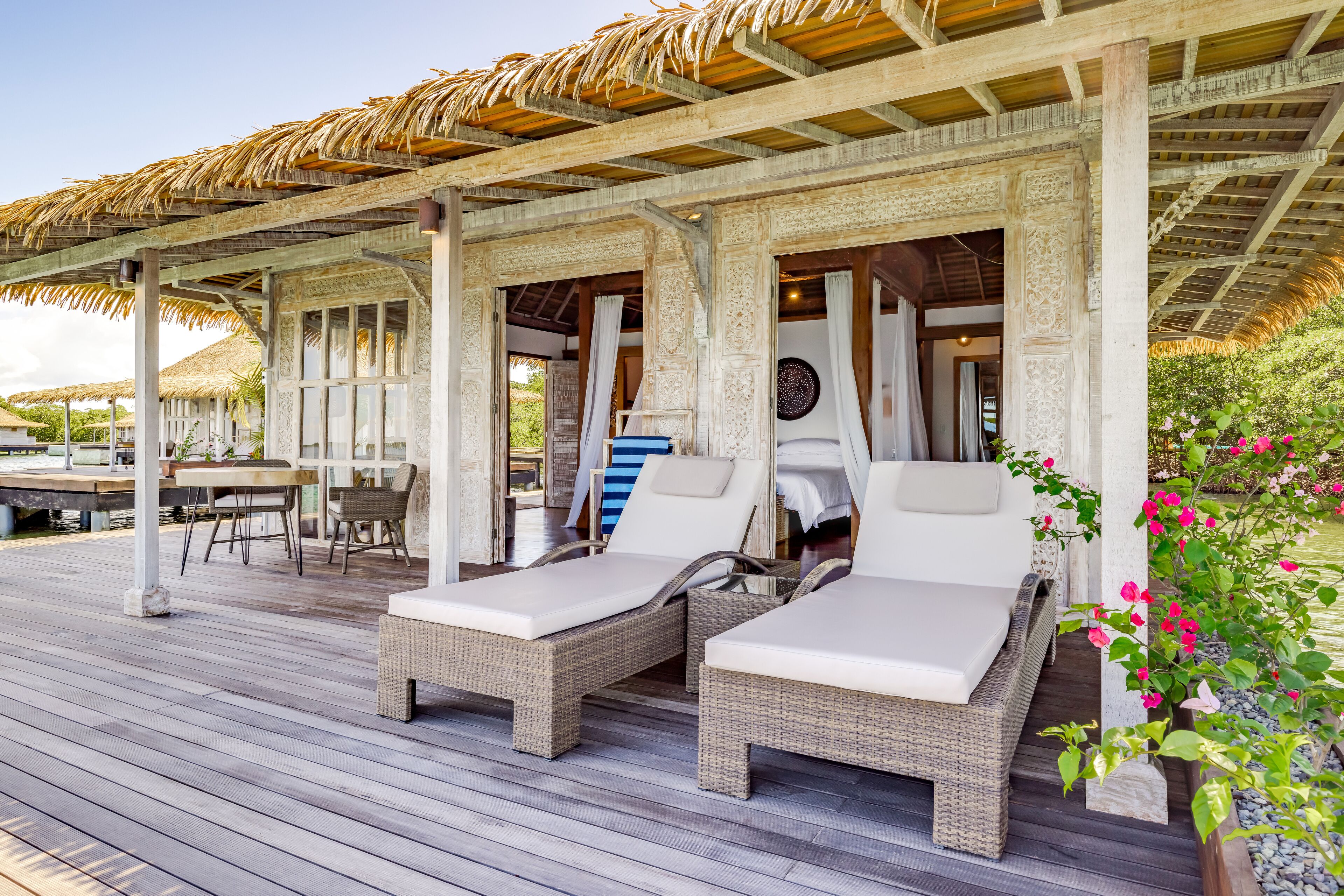 A covered outdoor area with two wicker lounge chairs and a dining table.