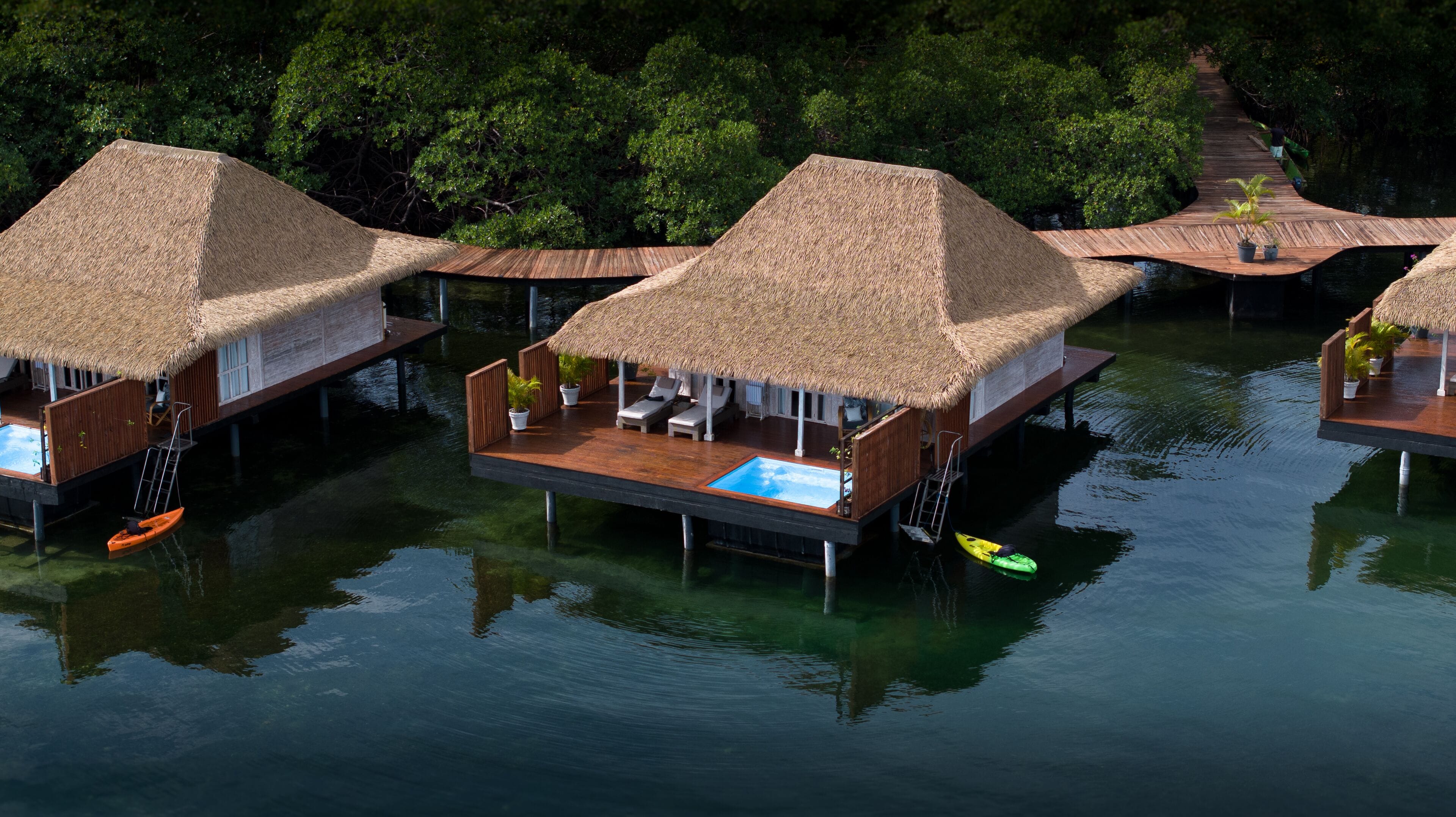Overwater bungalows with thatched roofs, wooden decks, and a small pool.