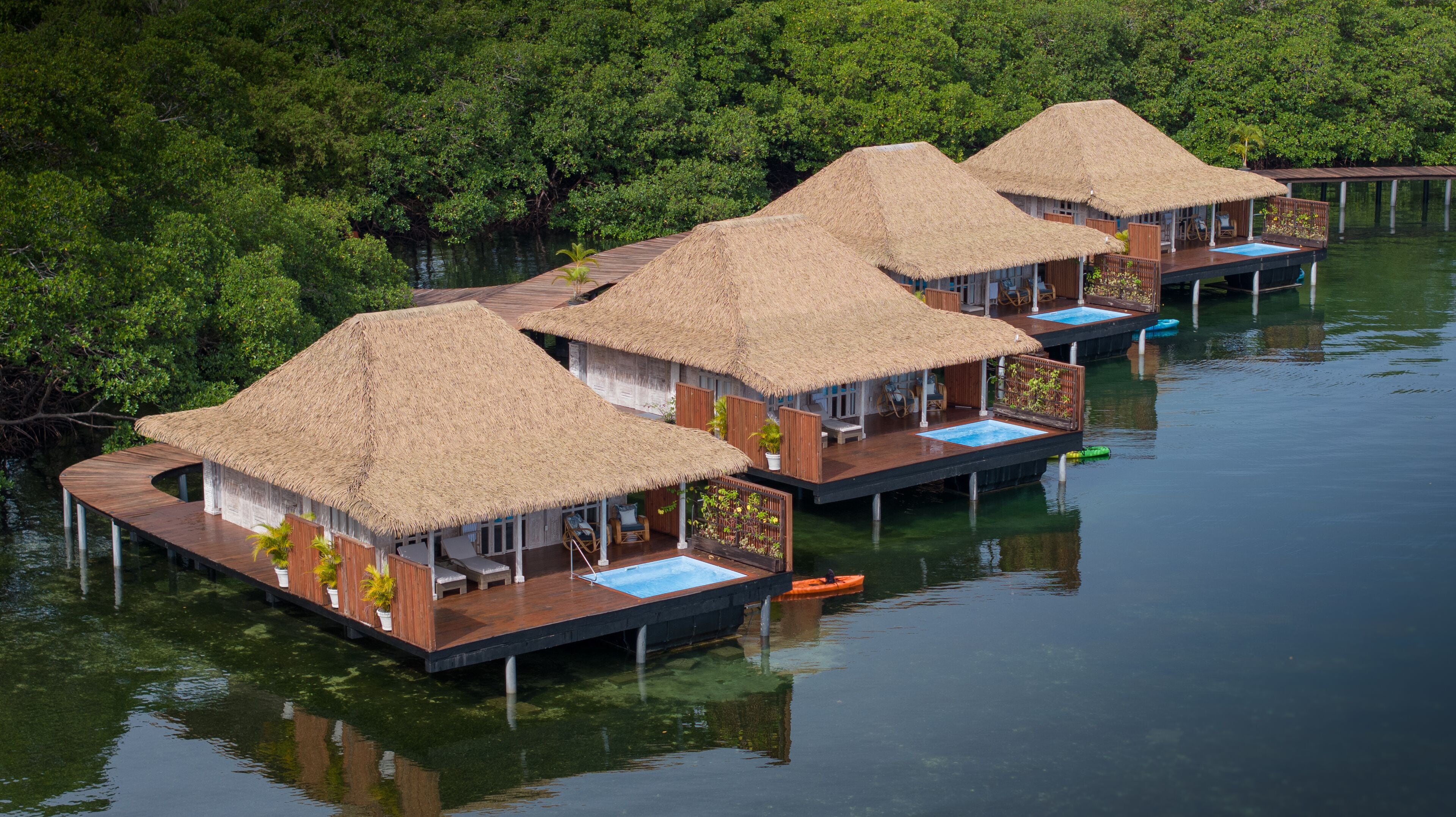 Overwater bungalows with thatched roofs, wooden decks, and private pools.