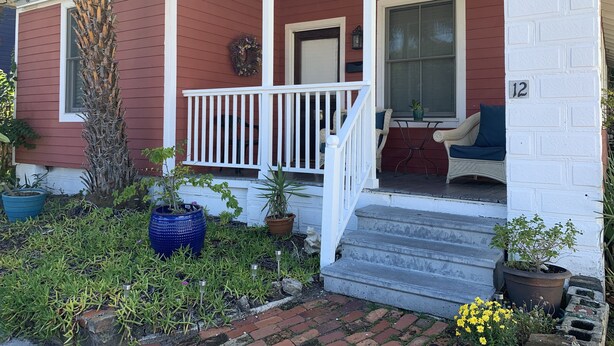 A red house with a white porch, steps leading to a door, and a number '12' on the wall. - Three Bedroom, Sanitized, Pet Friendly Bungalow (St. Augustine)