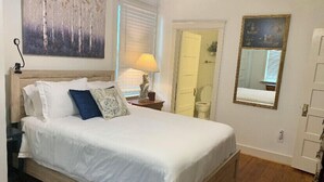 A neatly made bed with white bedding and decorative pillows, a bedside lamp, a wooden headboard, and a large abstract painting on the wall. - Three Bedroom, Sanitized, Pet Friendly Bungalow (St. Augustine)