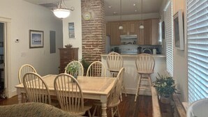 A dining area with a wooden table and chairs, a brick accent wall, and a kitchen in the background. - Three Bedroom, Sanitized, Pet Friendly Bungalow (St. Augustine)