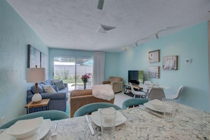 A spacious living area with a sofa, a dining table set for two, and a television.