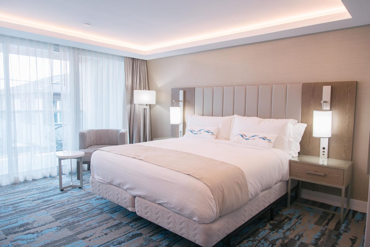 A hotel room with a large bed, a chair, a nightstand, and a lamp.