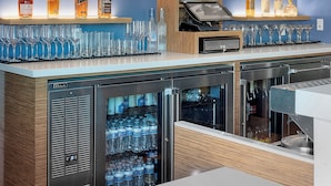 A bar area with shelves of liquor bottles, glasses, and a refrigerator stocked with water bottles. -  H2O Hermosa Beach Hotel (Hermosa Beach)