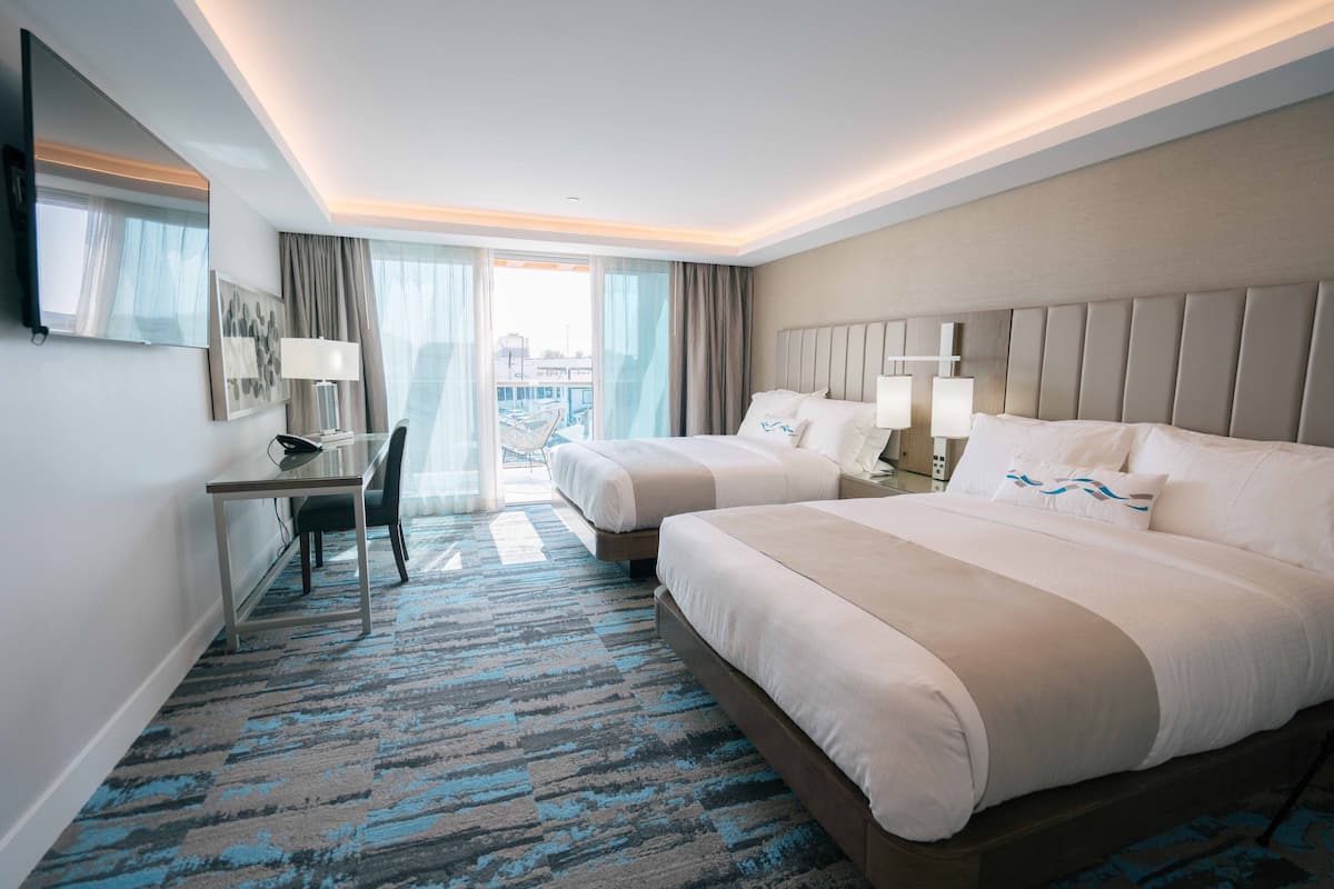 A hotel room with two beds, a desk, a chair, and a large window with curtains.