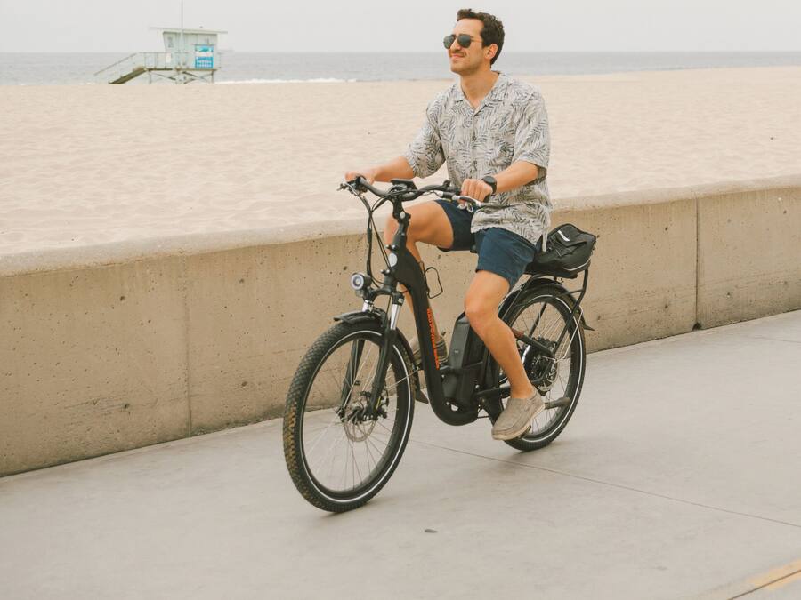 A person riding a stationary bike on a concrete path by the beach.