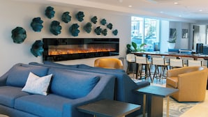 A modern lounge area with a blue sofa, a coffee table, and a flat-screen TV mounted on the wall. -  H2O Hermosa Beach Hotel (Hermosa Beach)