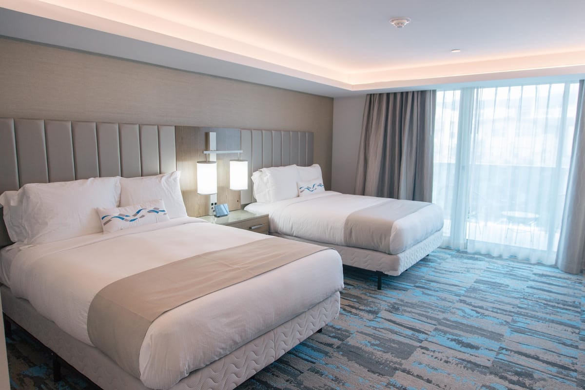 A hotel room with two beds, a large window with curtains, and a blue patterned carpet.
