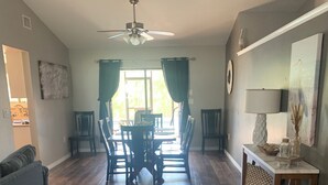 Un vaste salon comprenant un coin repas, un plancher en bois, un ventilateur de plafond et une vue sur l’extérieur.
