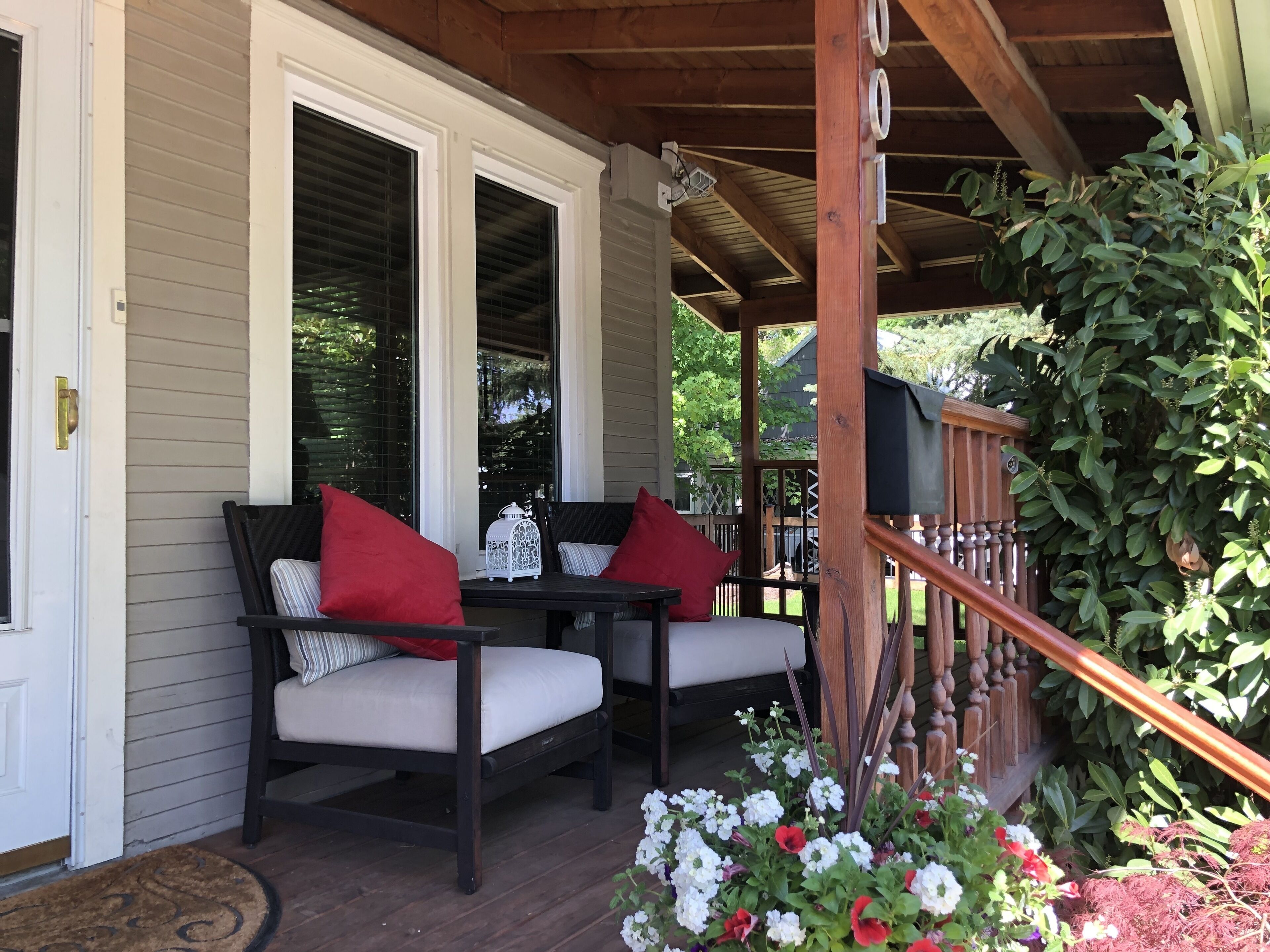 A porch with two chairs and a table, a wooden railing, and a mailbox.