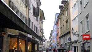 Una calle empedrada flanqueada por edificios de varios pisos, algunos con letreros visibles de comercios y restaurantes.