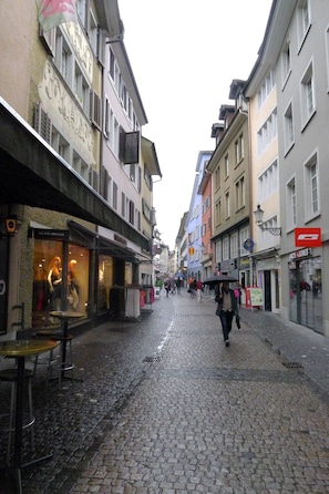 A cobblestone street lined with buildings, some with storefronts and signage. - In the heart of Zurich (Zürich)