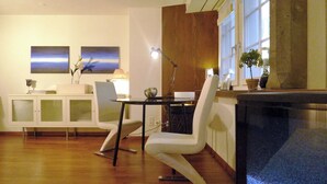 Un comedor moderno con suelo de madera, sillas blancas, una mesa de vidrio y dos cuadros en la pared.