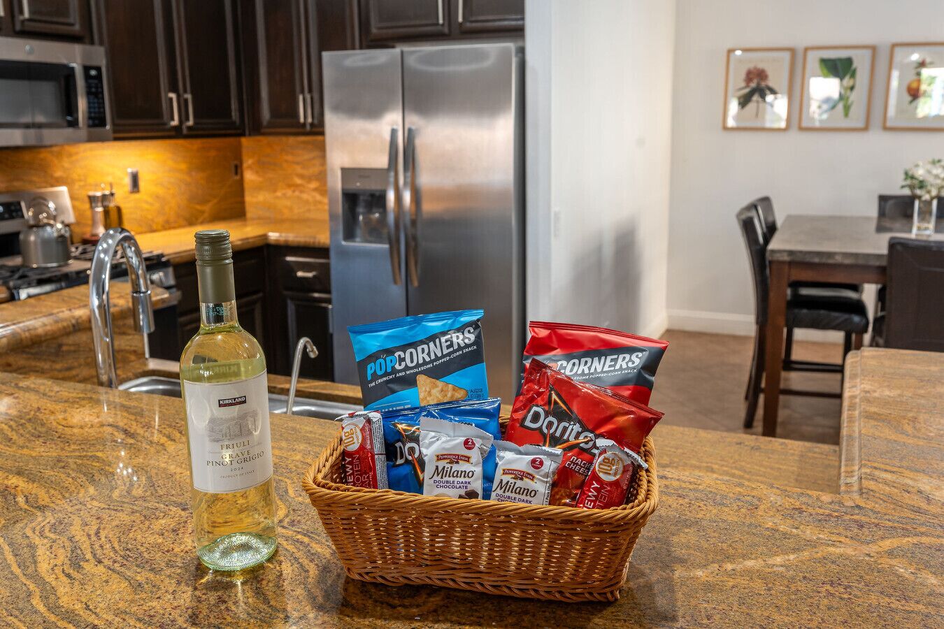 A kitchen counter with a bottle of wine, a basket of snacks, and a refrigerator.