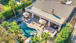 An aerial view of a house with a swimming pool, patio furniture, and palm trees.