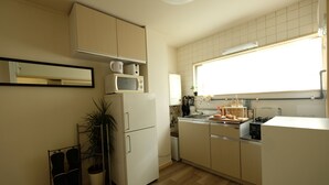 Eine moderne Küche mit weißen Schränken, einer Mikrowelle, einem Kühlschrank und einem Fenster mit Tageslicht.