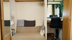 Um espaço compacto com sofá-cama, secretária pequena com computador e estante com espaço de armazenamento.