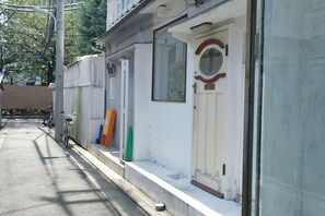 A narrow street with a row of white buildings, a bicycle, and a green cone. - COCO Nakameguro 301 (Tokyo)