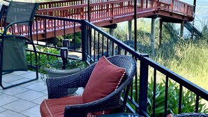 A terrace with wicker furniture and a glass table, overlooking a body of water and a distant shoreline.