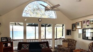 A spacious living room with a high ceiling, large windows, and a view of the outdoors.