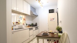 A compact kitchen with white cabinets, a microwave, and a small dining table with chairs. - COCO Shinjuku (Tokyo)