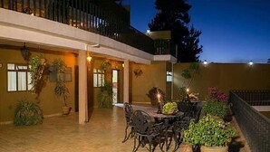 An outdoor patio area with a dining table and chairs, surrounded by potted plants and a railing.