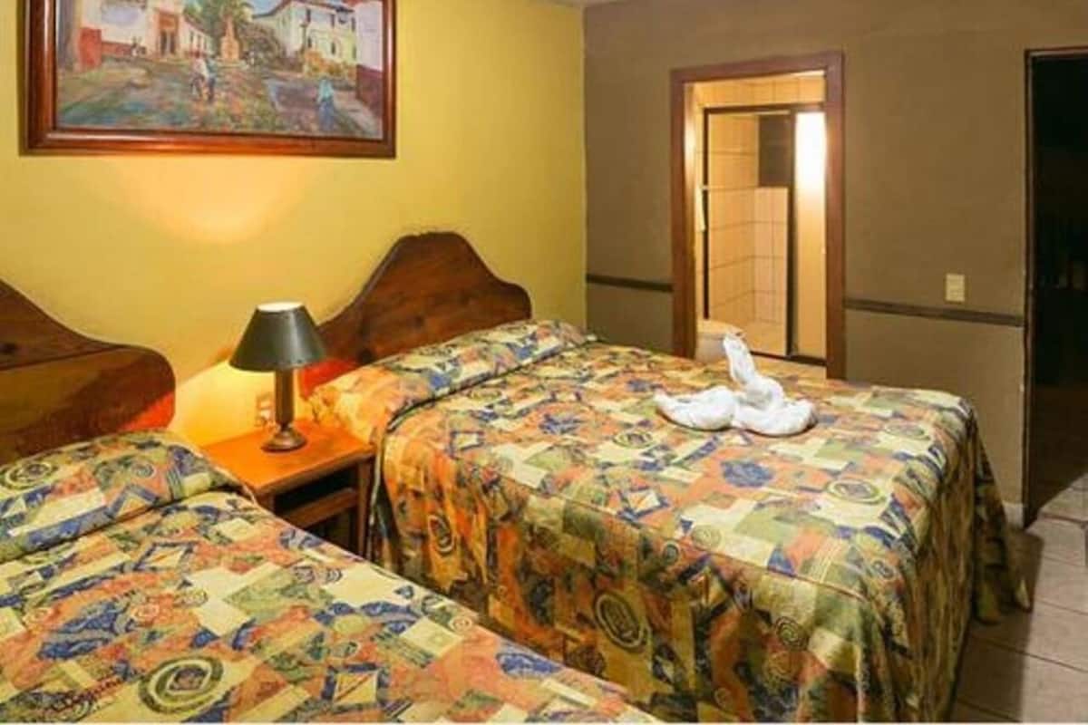 A hotel room with two beds, a nightstand, a lamp, and a painting on the wall.
