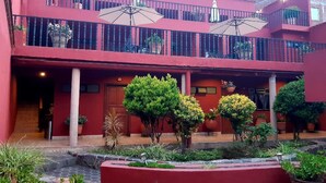 A red building with a covered outdoor seating area, potted plants, and a small water feature.