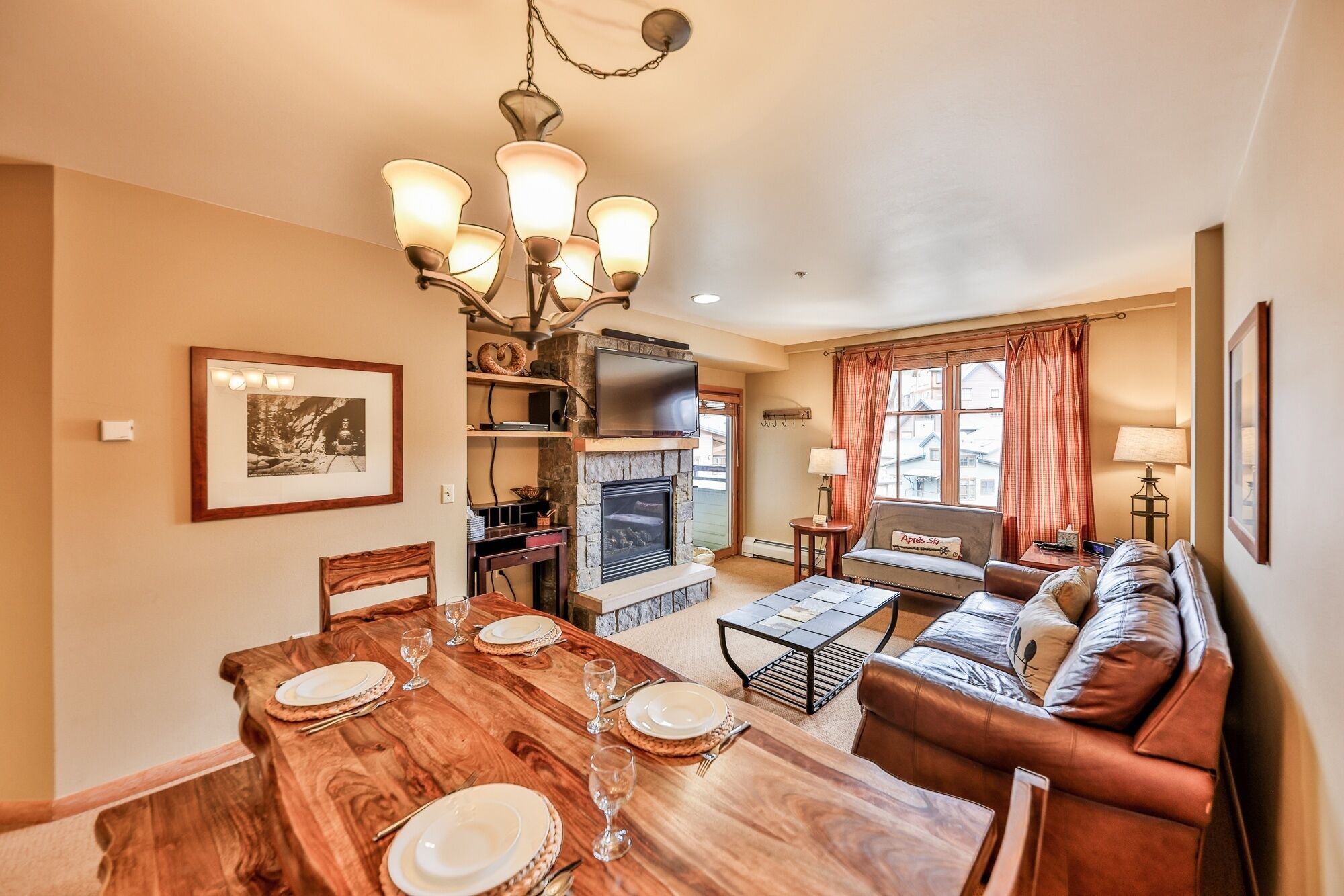 A cozy living room with a fireplace, a dining area with a wooden table set for four, and a comfortable seating area with a sofa and a TV.