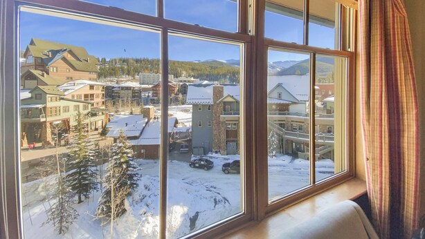 Une grande fenêtre à carreaux multiples, offrant une vue sur une ville enneigée avec des bâtiments et une montagne en arrière-plan.