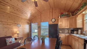 A wooden interior with a dining table, chairs, a sofa, a clock, and a refrigerator. - Wine Cup Rr9122wc 1 Bedroom Home by RedAwning (New Braunfels)