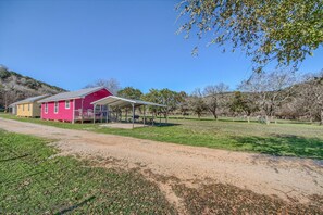 A pink building with a covered porch, surrounded by a grassy area and trees.