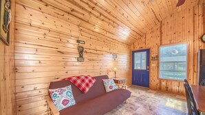 A cozy wooden cabin interior with a brown sofa, a small table, and a window with blinds. - Wine Cup Rr9122wc 1 Bedroom Home by RedAwning (New Braunfels)