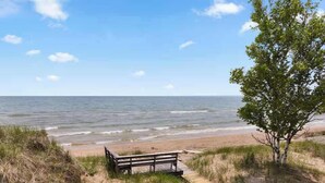 A bench on a sandy path leading to a beach with the ocean in the background. - Stunning Lakefront 5BR 5000 sq ft Dune Alright (Baileys Harbor)