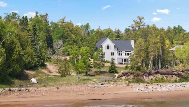 A house with a large porch, surrounded by trees and a beach. - Stunning Lakefront 5BR 5000 sq ft Dune Alright (Baileys Harbor)