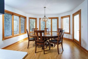 A dining room with a round table, six chairs, and large windows.