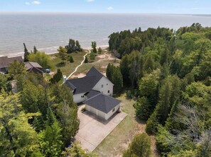 A house with a large driveway, surrounded by dense trees and a view of the ocean.