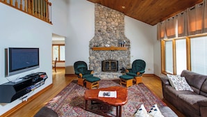 A living room with a stone fireplace, wooden ceiling, and a television on the wall. - Stunning Lakefront 5BR 5000 sq ft Dune Alright (Baileys Harbor)