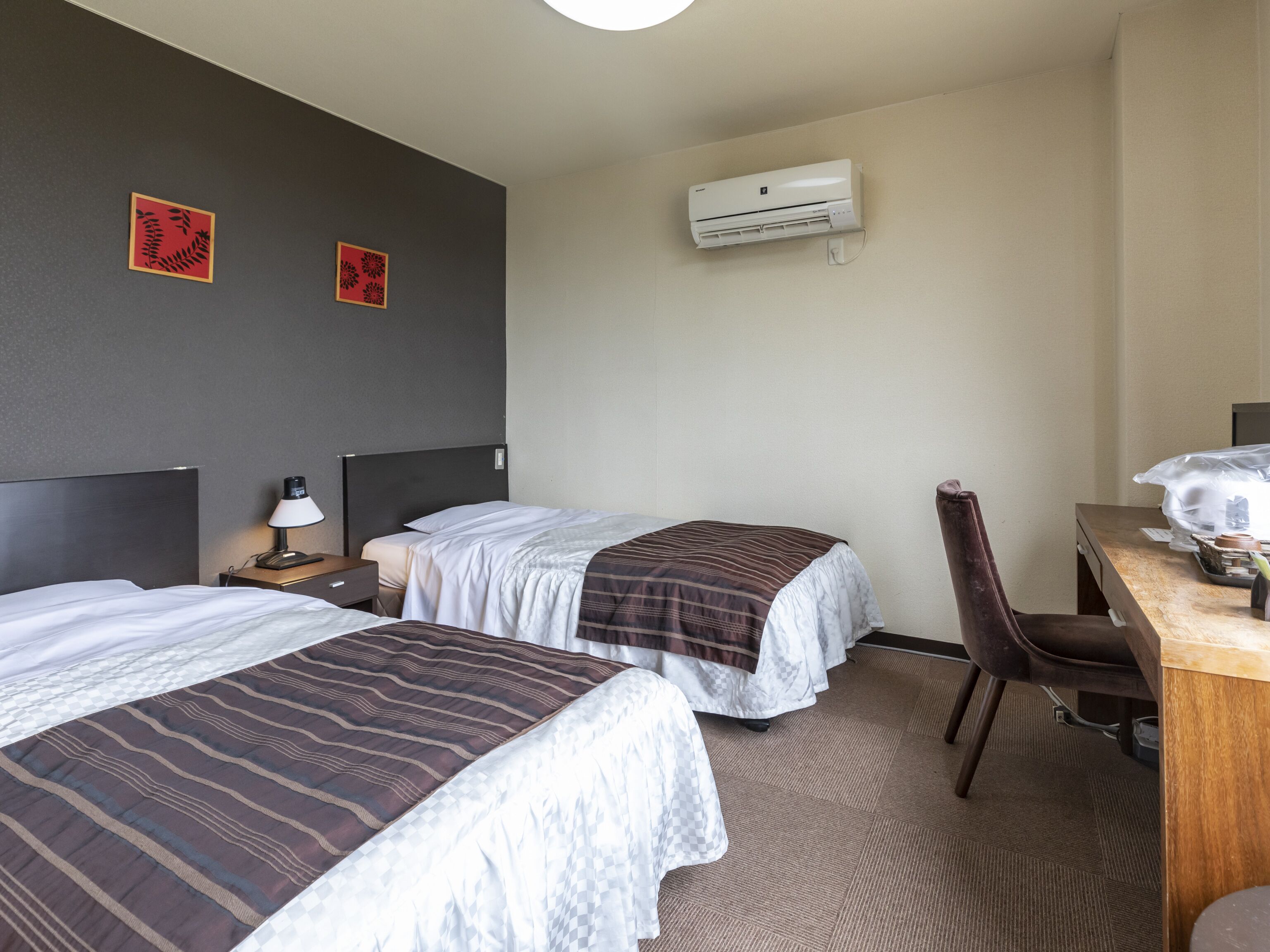 Habitación de hotel con dos camas, un escritorio, una silla, aire acondicionado y dos adornos de pared.
