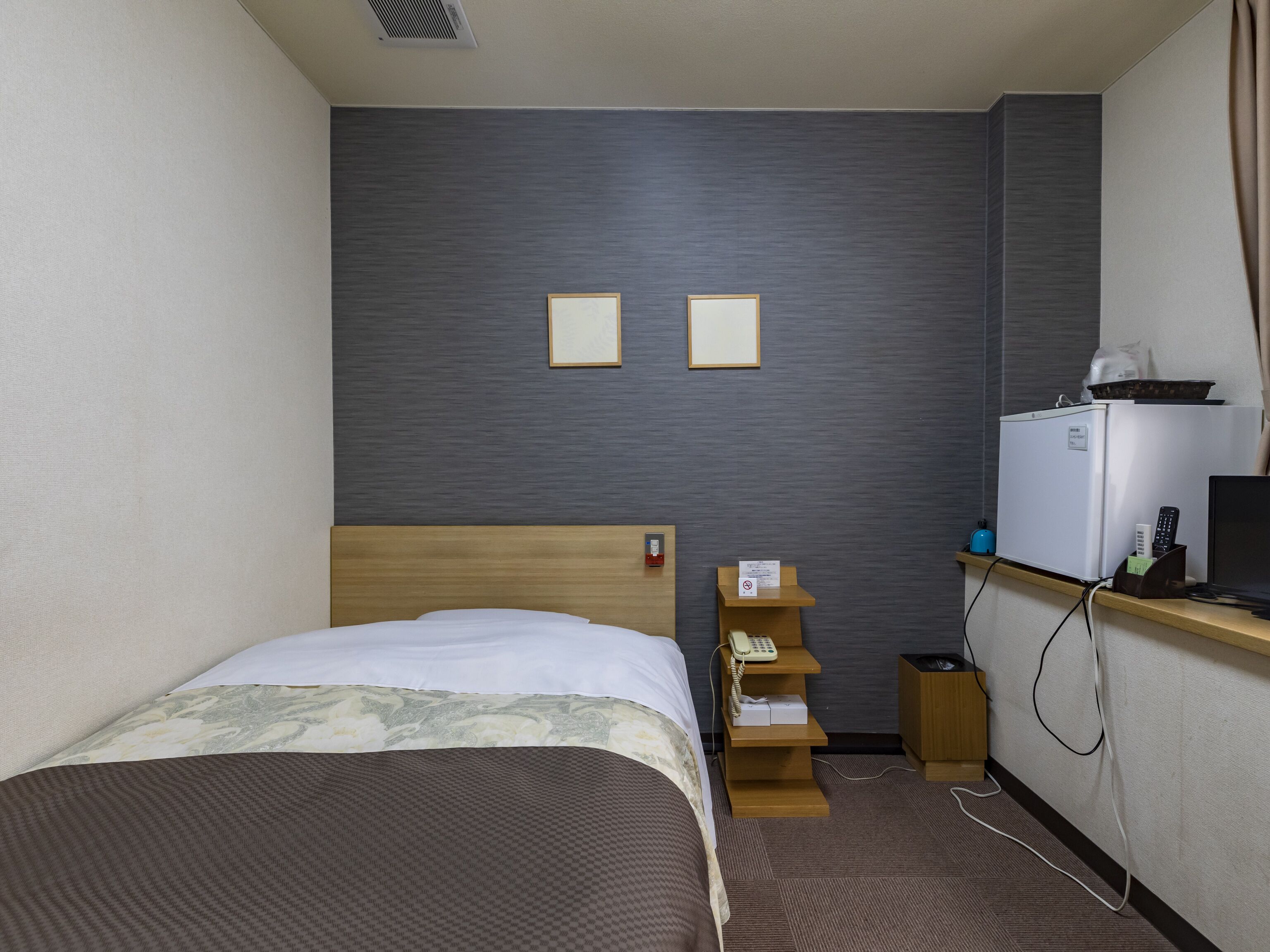 A hotel room with a bed, a desk with a computer, a phone, and a small refrigerator.