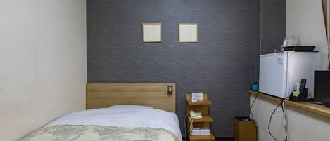 A hotel room with a bed, a desk with a computer, a phone, and a small refrigerator.