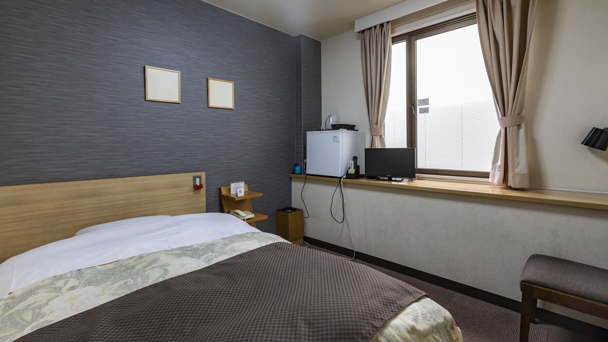 Hotelkamer met een bed, een bureau met computer, een kleine koelkast en een raam met gordijnen.